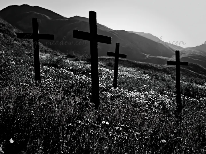 Three rustic crosses are placed in a meadow during Christmas season. The sun sets behind the mountains, casting a backlight that highlights the silhouettes of t