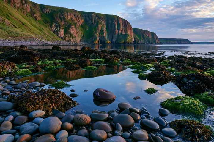 Tide pools reflect the sky along a rocky coastline beneath dramatic cliffs.