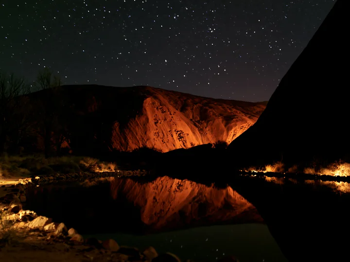 Uluru under a starry night sky shows the famous rock formation illuminated by natural light.