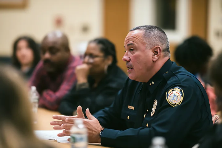 Uniformed police chief speaks at a table during a civilian oversight meeting with community members.