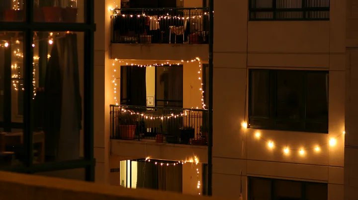 Warm Christmas lights decorate balconies and windows on a residential apartment building at night.