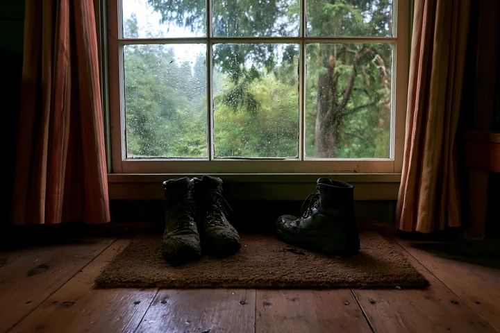 Worn boots sit on a mat inside a cabin near a window.